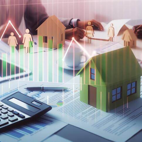 Imagem mostra uma mesa com vários relatórios, calculadora e caneta com uma casa pequena em cima da mesa